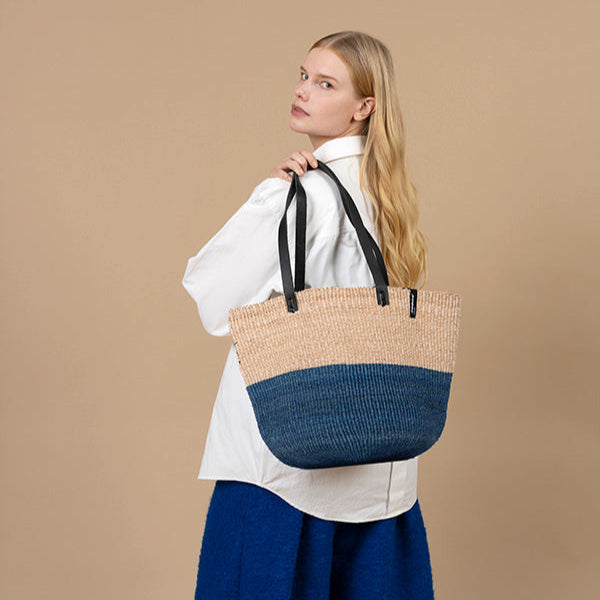Woman holding a two-toned straw handmade and fair trade bag against a beige background