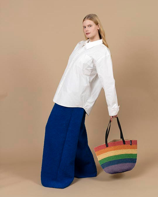 Woman holding a rainbow tote bag against a beige background