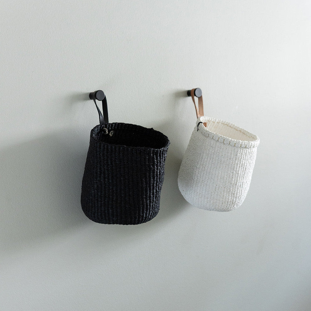 Two woven baskets, one black and one white, hanging on a plain wall.