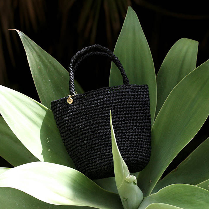 Black woven handbag on a large green leaf