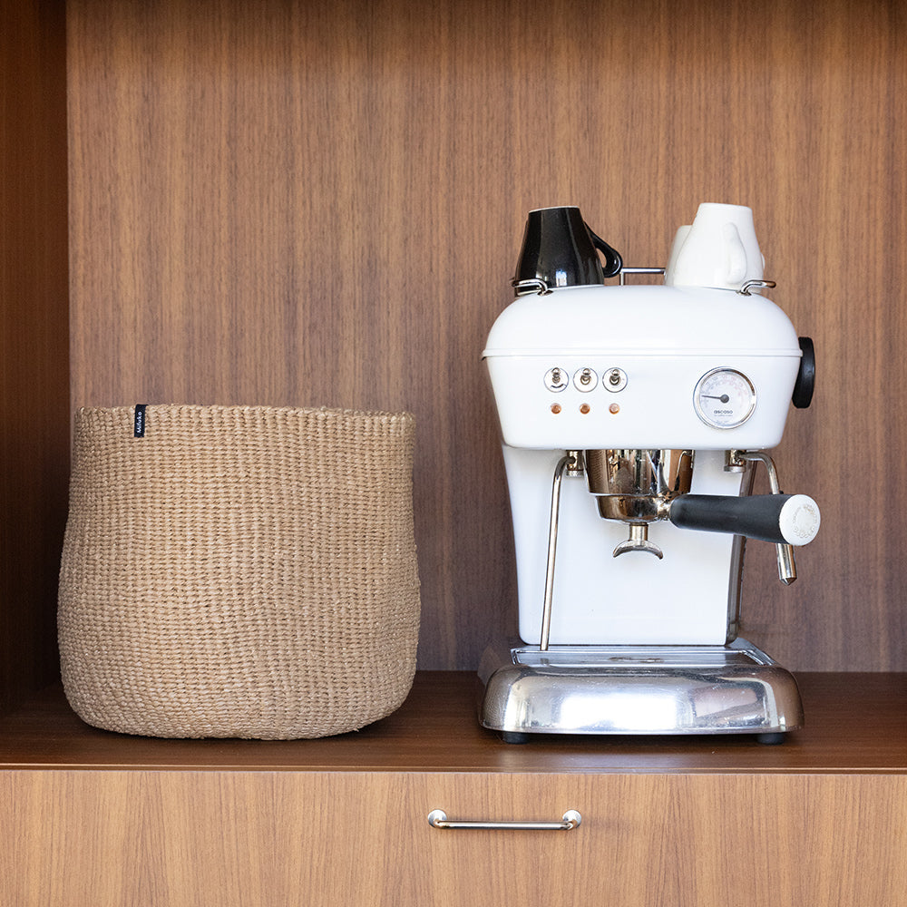 White espresso machine on a wooden cabinet with a woven basket next to it.