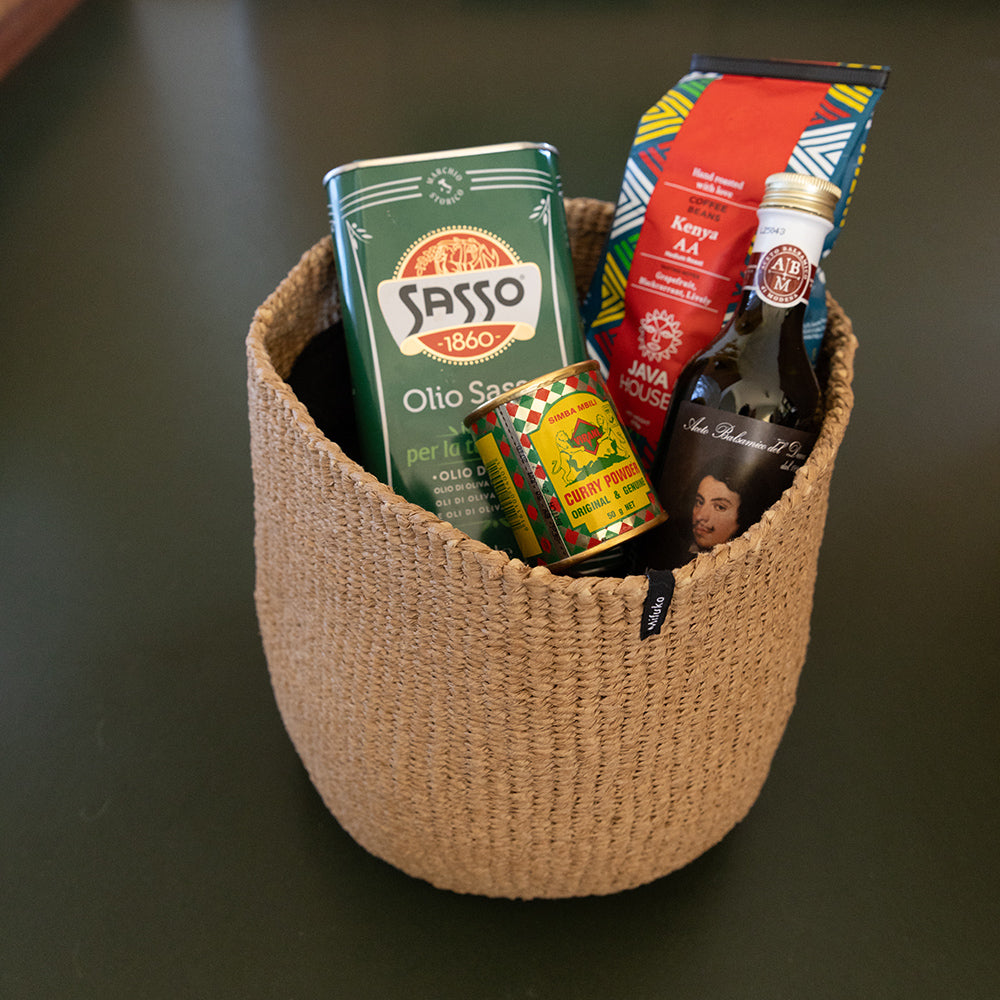 Woven basket with assorted food items including a green can and red package on a dark surface