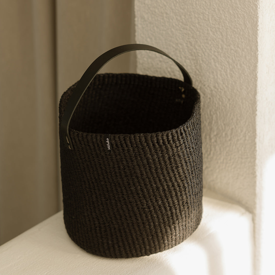Black woven basket with handle on a light surface
