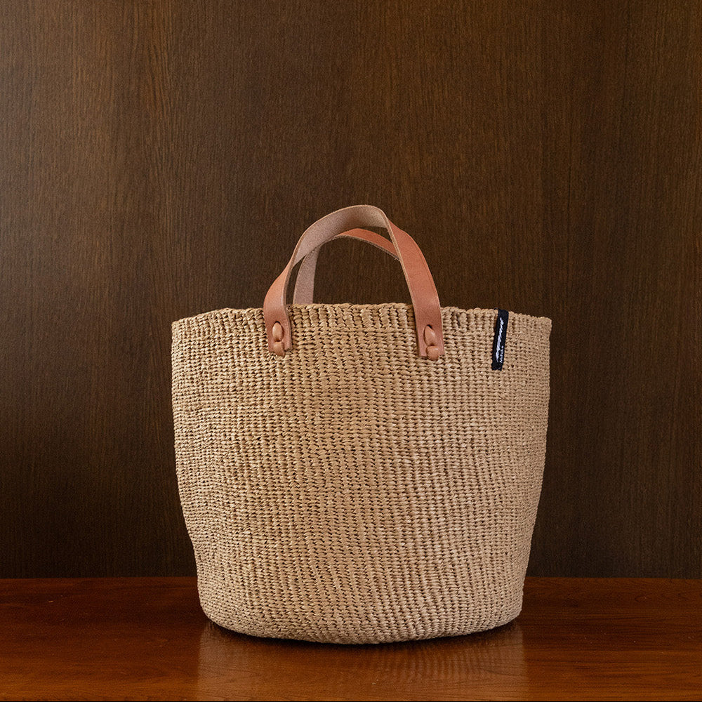Woven basket with leather handles on a wooden surface against a brown background