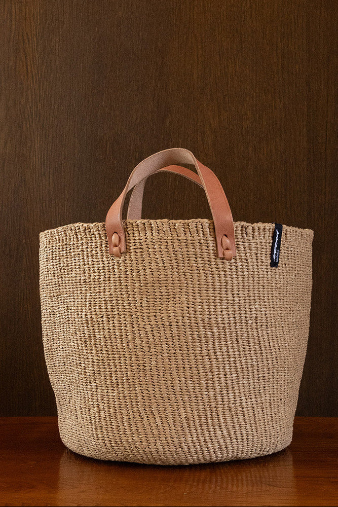 Woven basket with leather handles on a wooden surface against a brown background
