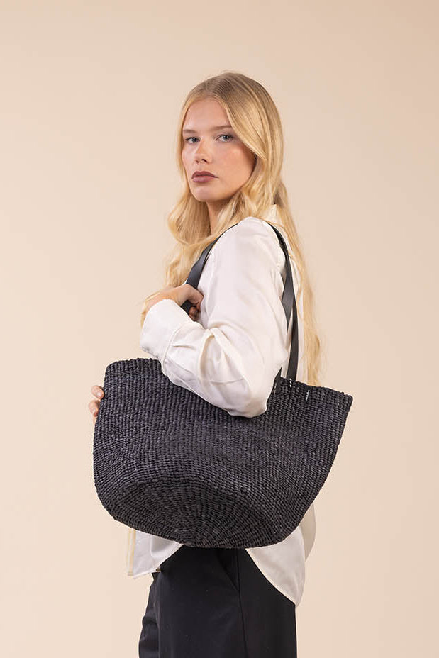 Woman holding a textured black handbag against a beige background