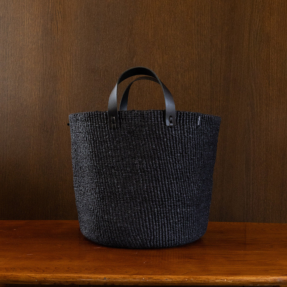Textured black tote bag with leather handles on a wooden surface against a brown background