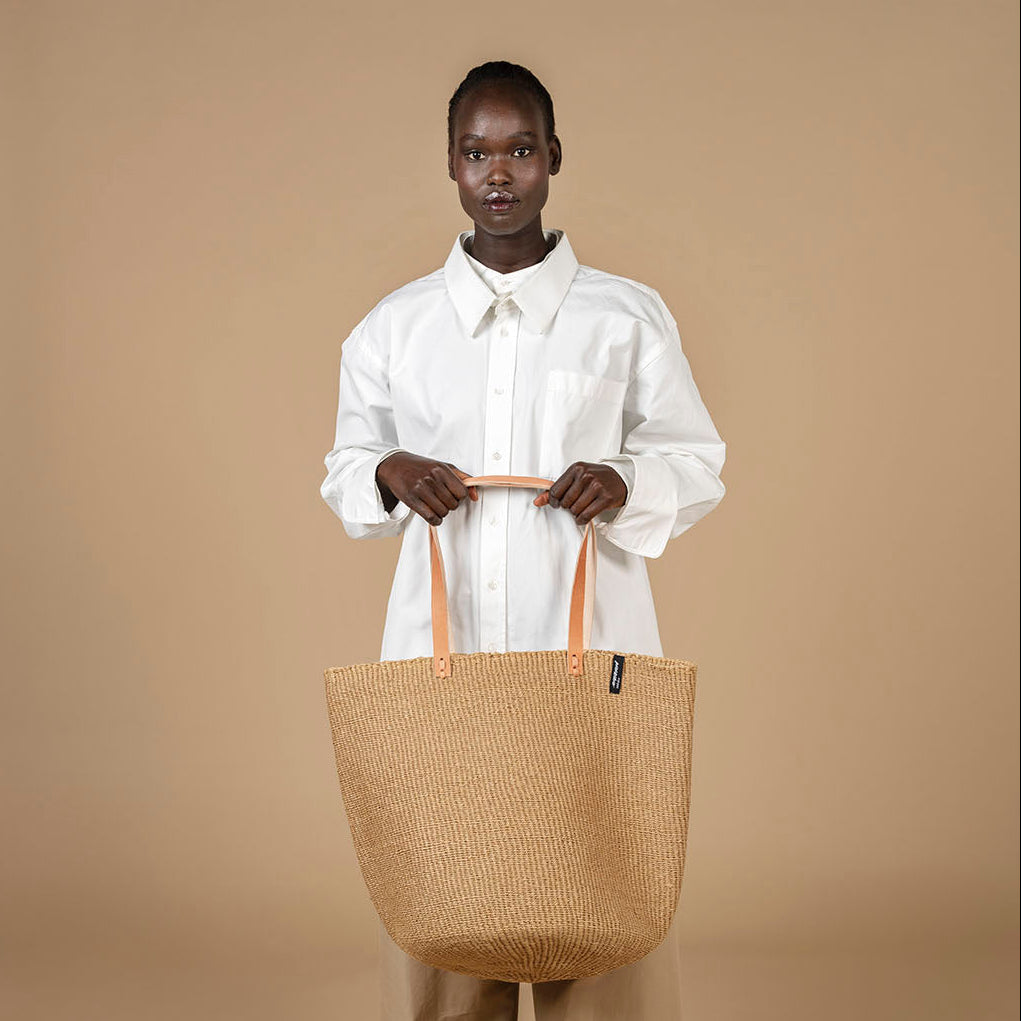 Woman holding big brown shopper with leather handles. Wearing white shirt.