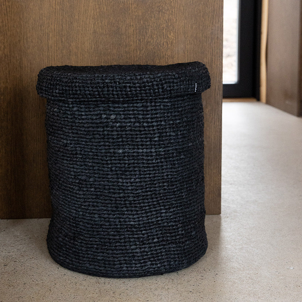Black woven basket against a wooden wall.