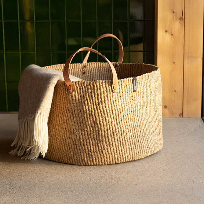 big brown floor basket with leather handles and blanket.