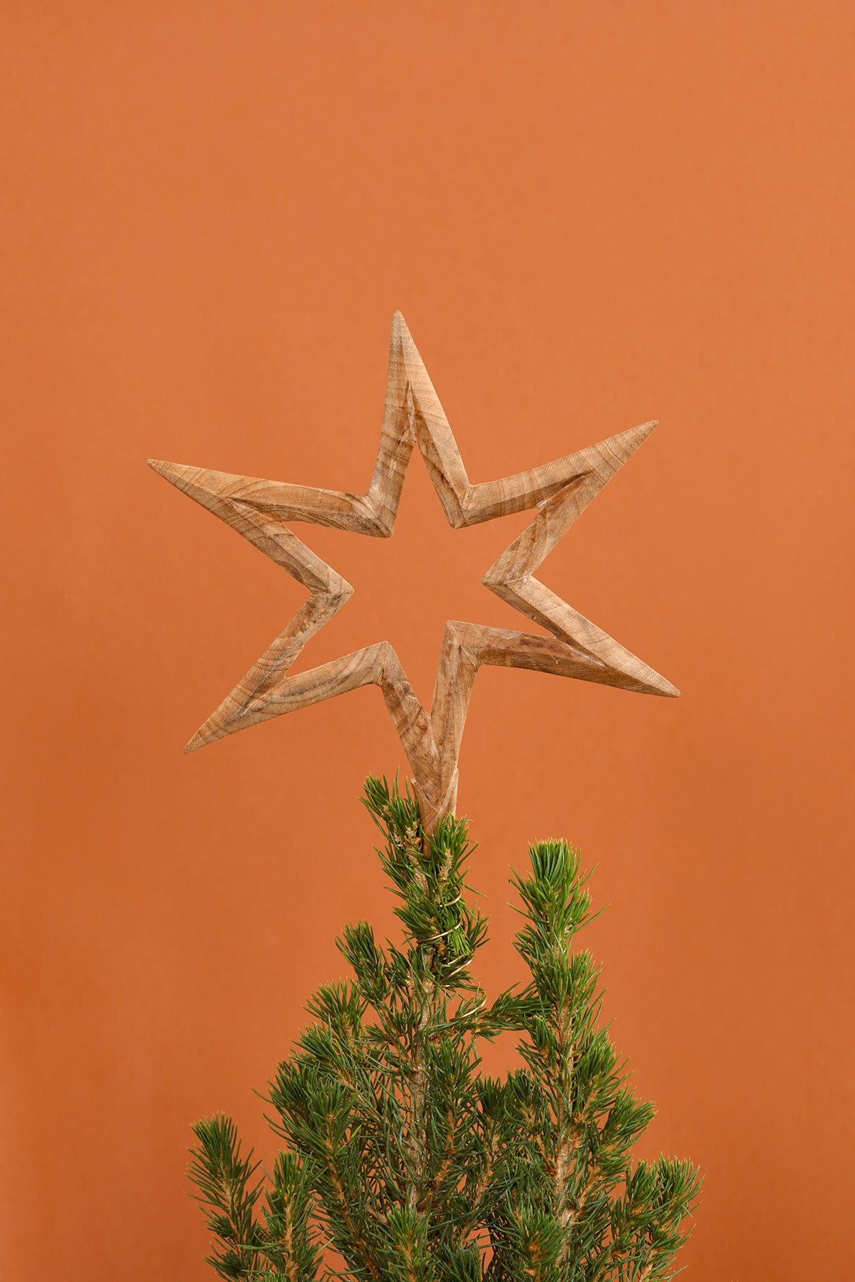 Wooden star tree topper on a Christmas tree against an orange background