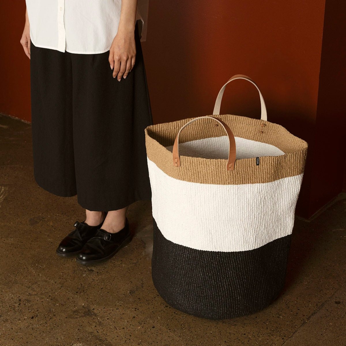 The Kiondo floor basket in Duo Black is a stunning and functional storage solution that seamlessly blends traditional craftsmanship with modern design. Handwoven by skilled artisans, this extra-large basket is crafted from a durable mix of FSC-certified paper and recycled plastic, ensuring it is lightweight, strong, and environmentally friendly.