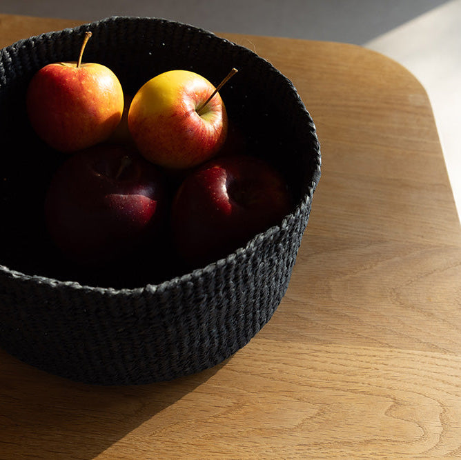 Black woven basket with apples on a wooden surface