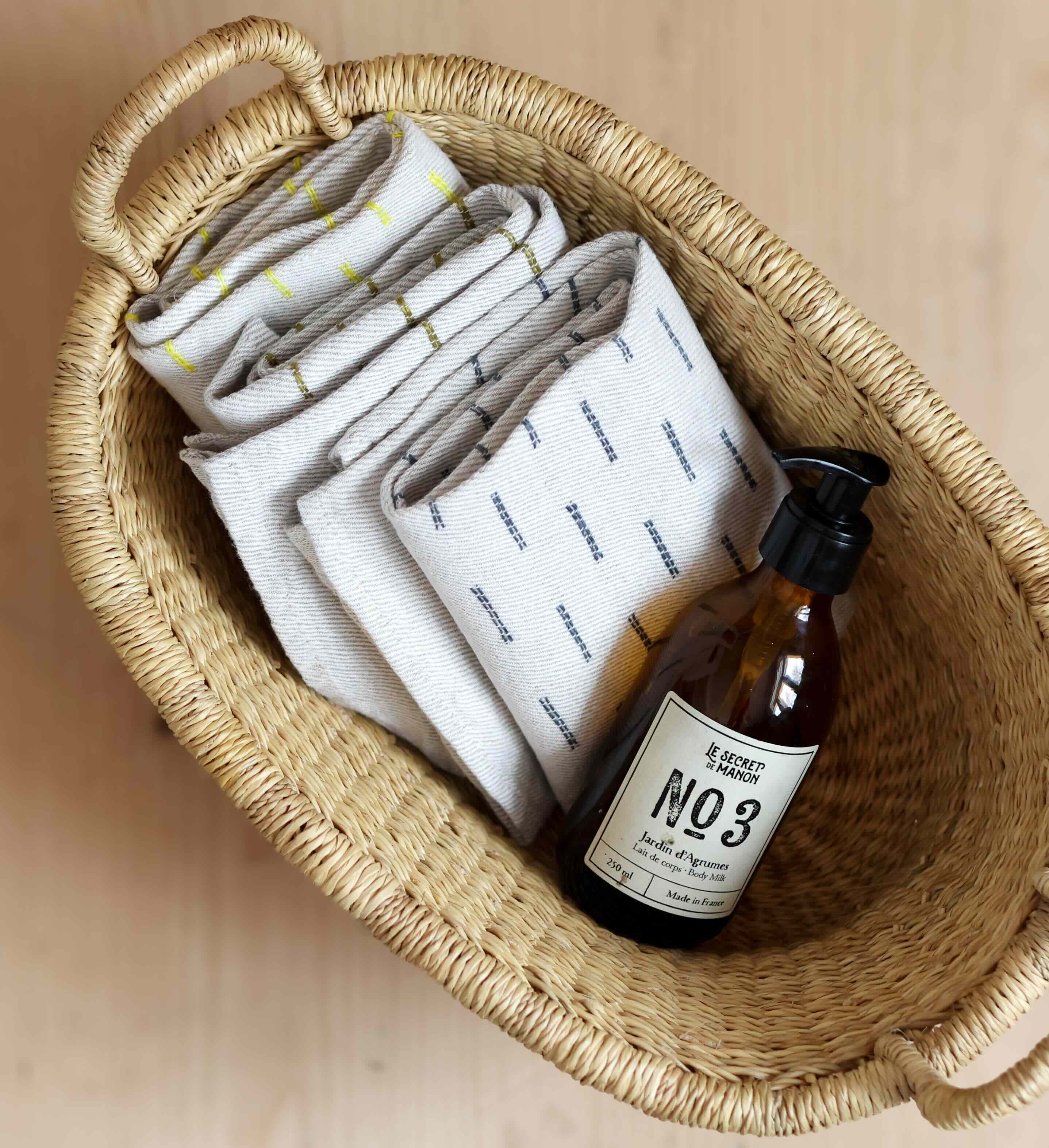 Wicker basket with folded towels and a bottle labeled 'No. 3' on a neutral background