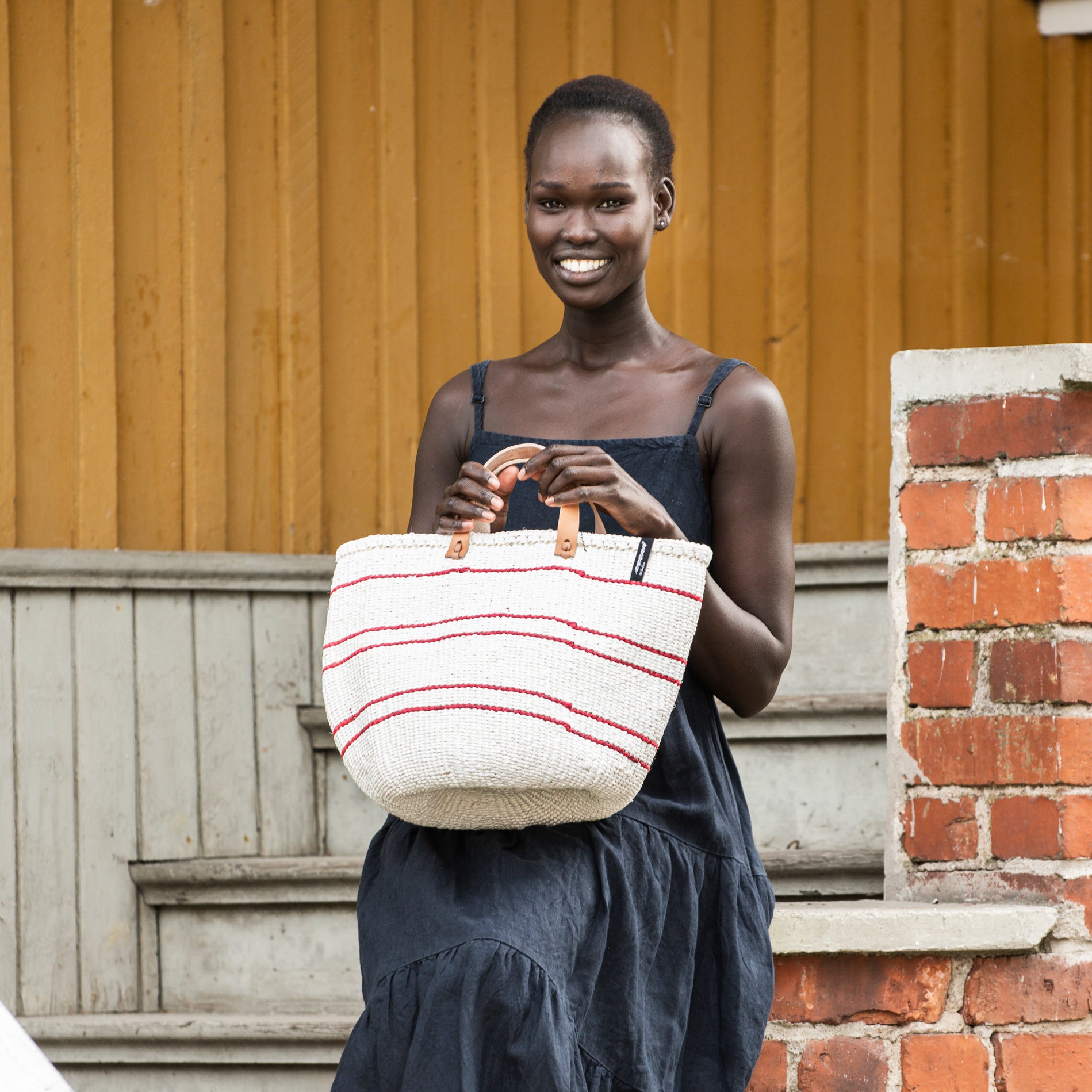 Woman modelling Kiondo market basket from Mifuko's 5 Red Lines collection.