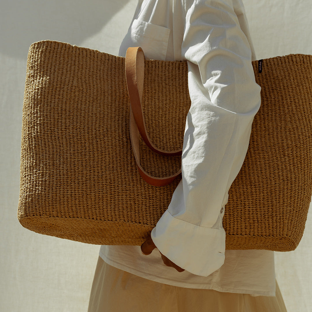 Person holding a woven brown bag against a plain background