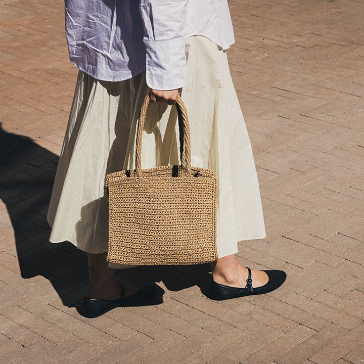 Person holding a woven bag on a brick pavement