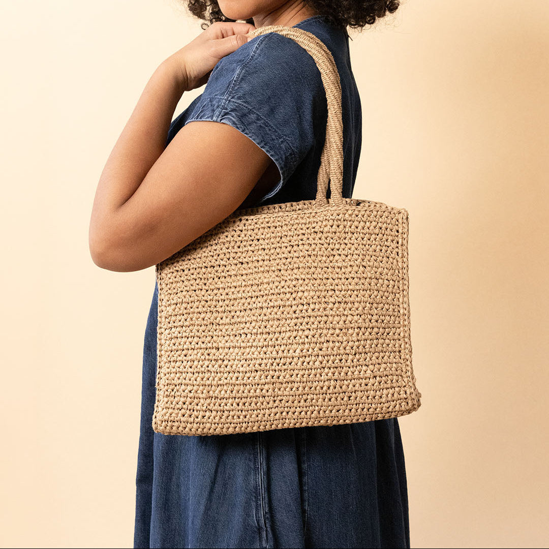 Woman holding a crocheted tote bag against a beige background