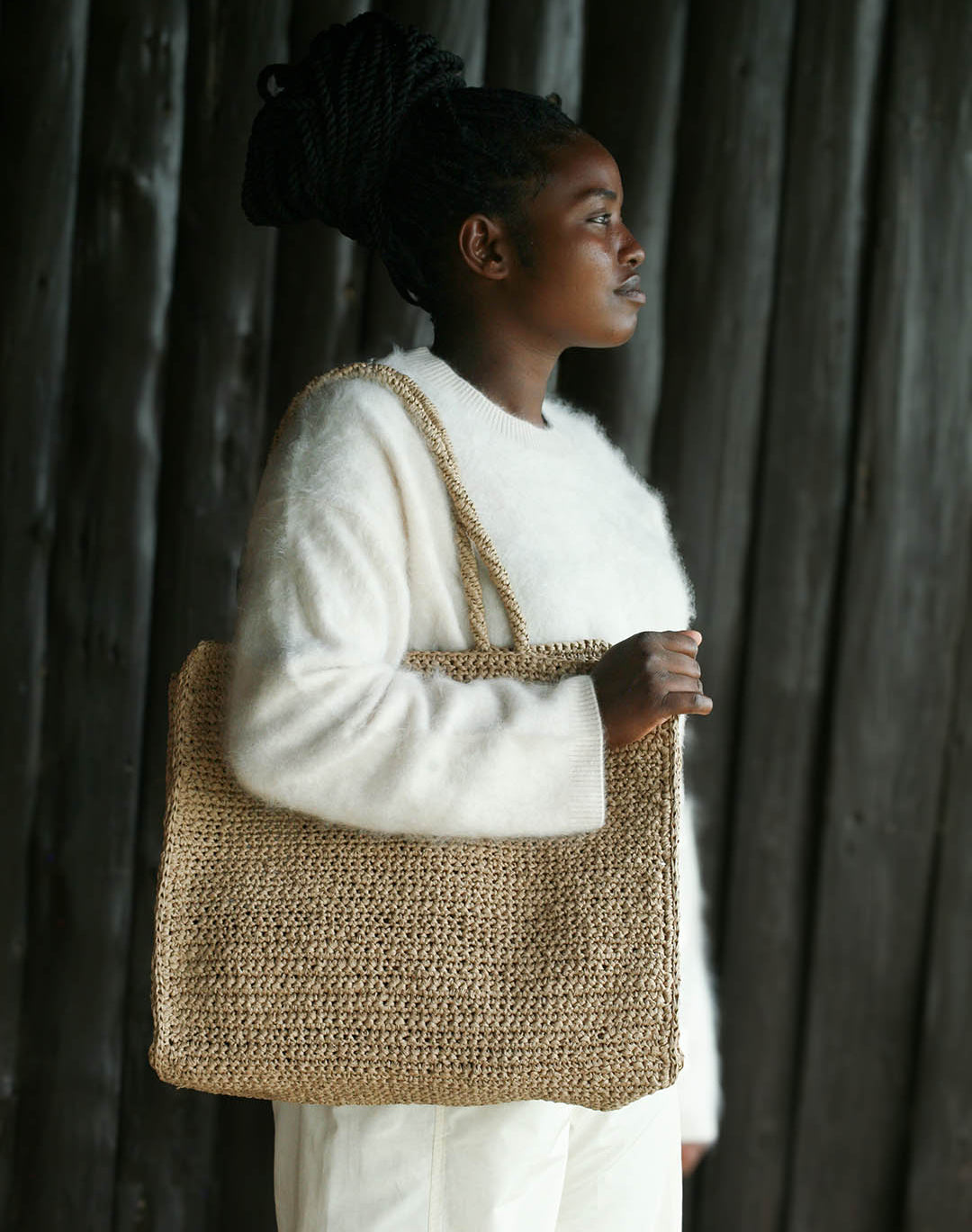 Woman holding a woven bag against a dark curtain background
