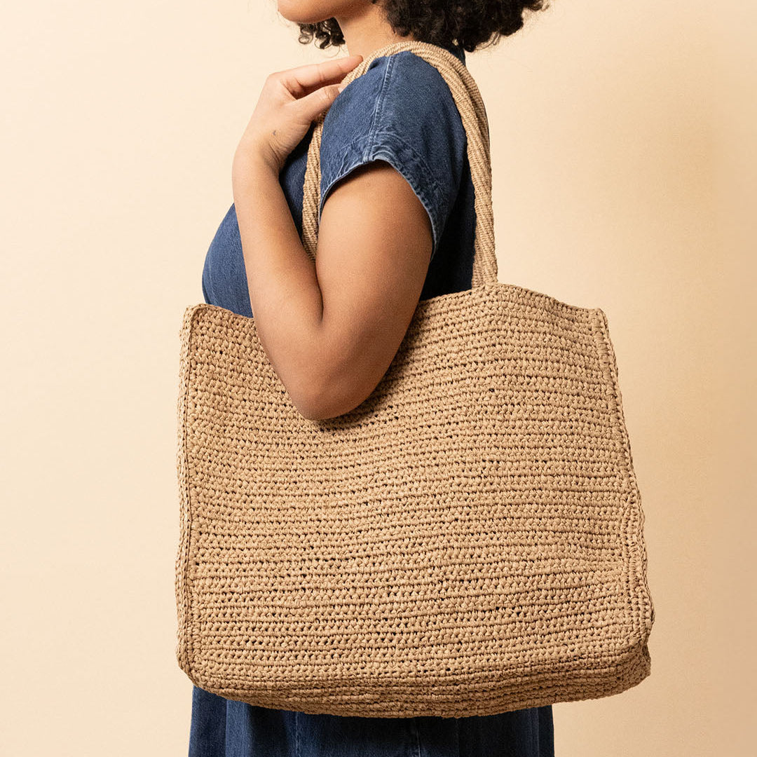 Woman holding a woven tote bag against a beige background